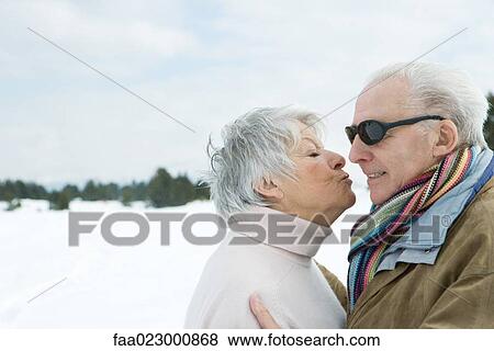 Stock Photo - Senior couple standing face to face, kissing, side view. Fotosearch