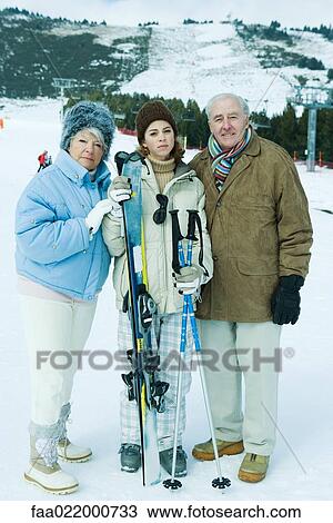 Stock Image - Senior couple standing on ski slope with teen granddaughter holding ski gear. Fotosearch