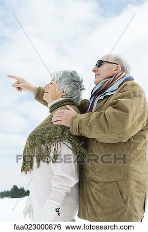 Stock Photograph - Senior couple standing together, looking up, man pointing. Fotosearch