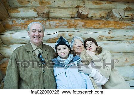Stock Photograph - Senior couple standing with teen and preteen granddaughters in front of log cabin, smiling, portrait. Fotosearch