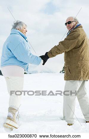 Senior couple walking together, holding hands, man looking over shoulder at camera View Large Photo Image Stock Image - Senior couple walking together, holding hands, man looking over shoulder at camera. Fotosearch
