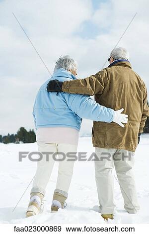 Stock Photo - Senior couple walking together in snow, full length, rear view. Fotosearch