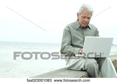 Senior man sitting outdoors, using laptop computer, looking down View Large Photo Image Stock Image - Senior man sitting outdoors, using laptop computer, looking down. Fotosearch