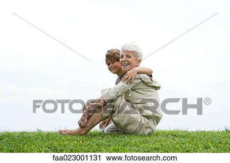 Senior woman and grandson sitting on grass, smiling at camera, full length View Large Photo Image Stock Image - Senior woman and grandson sitting on grass, smiling at camera, full length. Fotosearch