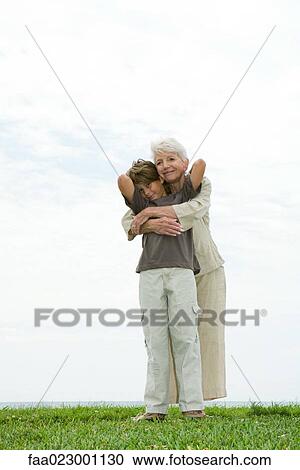 Senior woman and grandson standing on grass, embracing, smiling at camera, full length View Large Photo Image Stock Image - Senior woman and grandson standing on grass, embracing, smiling at camera, full length. Fotosearch