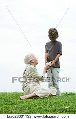 Senior woman sitting on grass, grandson handing her gift, full length View Large Photo Image Stock Image - Senior woman sitting on grass, grandson handing her gift, full length. Fotosearch