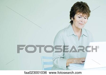 Stock Photograph - Senior woman using laptop computer, looking down, smiling. Fotosearch