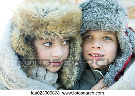 Stock Photo - Sister and brother wearing fur caps, smiling, looking away, portrait. Fotosearch