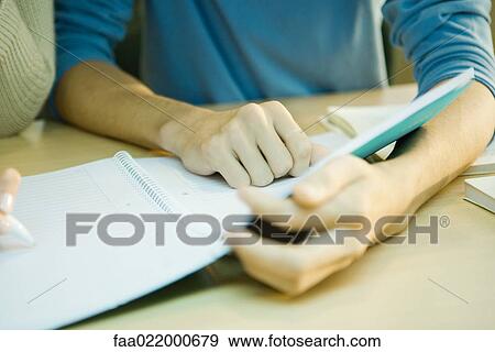 Stock Photo - Students studying together in university library, close-up of young man's arms holding notebook . Fotosearch