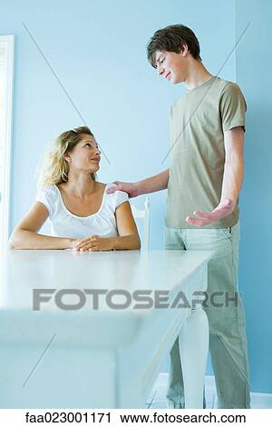 Teen boy standing next to mother sitting at table, hand on her shoulder, gesticulating View Large Photo Image Stock Image - Teen boy standing next to mother sitting at table, hand on her shoulder, gesticulating. Fotosearch
