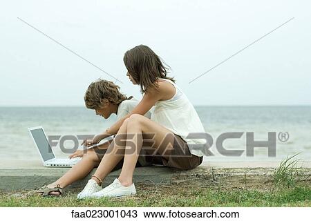 Teen girl and little brother sitting on the ground, using laptop computer, one pointing and looking over the other's shoulder View Large Photo Image Stock Image - Teen girl and little brother sitting on the ground, using laptop computer, one pointing and looking over the other's shoulder. Fotosearch