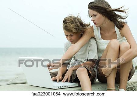 Picture - Teen girl and little brother using laptop computer together, girl pointing over boy's shoulder. Fotosearch