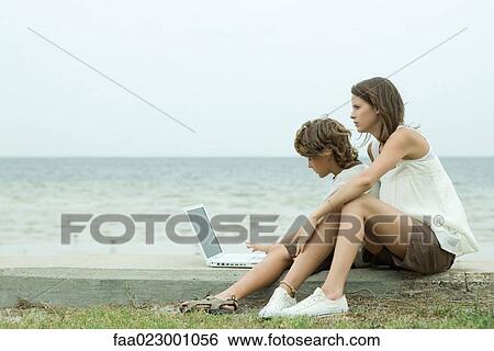 Teen girl and little brother using laptop computer together by ocean, side view View Large Photo Image Stock Photograph - Teen girl and little brother using laptop computer together by ocean, side view. Fotosearch