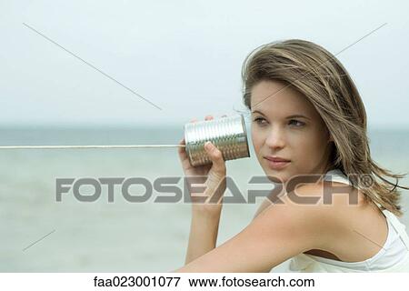 Stock Photo - Teen girl holding tin can phone up to ear, looking away, portrait. Fotosearch