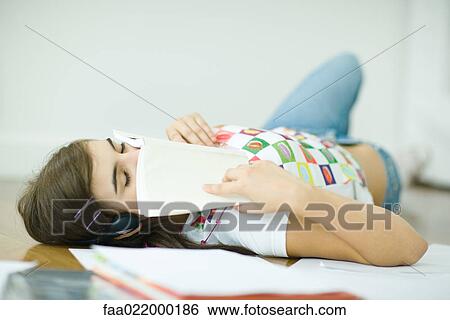 Stock Photograph - Teen girl lying on floor, doing homework, eyes closed and book over lower face. Fotosearch
