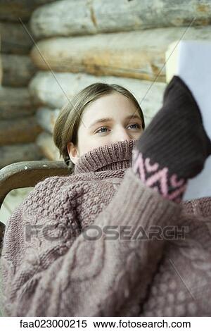 Stock Photography - Teen girl reading book while sweater neck covers mouth. Fotosearch