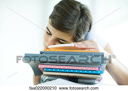 Stock Image - Teen girl resting head on stack of homework, eyes closed. Fotosearch