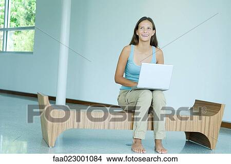 Picture - Teen girl sitting on bench, using laptop computer, smiling, looking up. Fotosearch