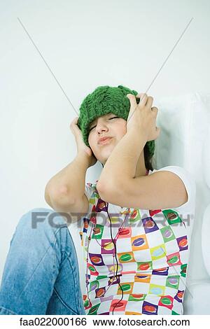 Stock Photograph - Teen girl wearing hat and headphones, eyes closed and hands over ears. Fotosearch