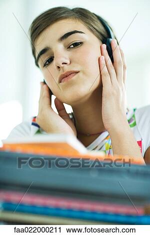 Stock Image - Teen girl with stack of homework, listening to headphones, portrait. Fotosearch