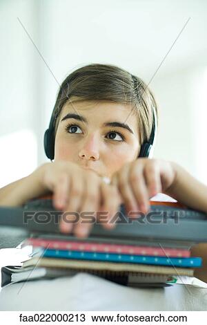Stock Image - Teen girl with stack of homework, listening to headphones, portrait. Fotosearch