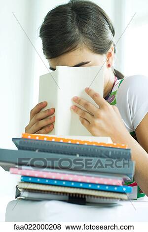 Teen girl with stack of homework, hiding face behind book, portrait View Large Photo Image Stock Photo - Teen girl with stack of homework, hiding face behind book, portrait. Fotosearch