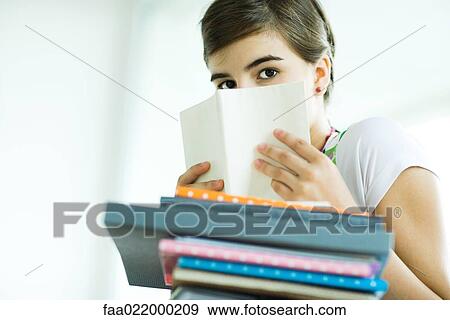 Stock Photo - Teen girl with stack of homework, hiding face behind book, portrait. Fotosearch