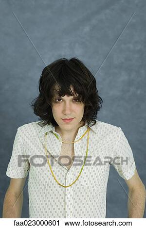 Stock Image - Teenage boy with hair in face, looking at camera, portrait. Fotosearch