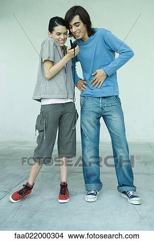 Teenage couple looking at cell phone together, full length portrait View Large Photo Image Picture - Teenage couple looking at cell phone together, full length portrait. Fotosearch