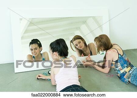 Teenage girl and young woman lying on ground, looking at selves in mirror View Large Photo Image Picture - Teenage girl and young woman lying on ground, looking at selves in mirror. Fotosearch