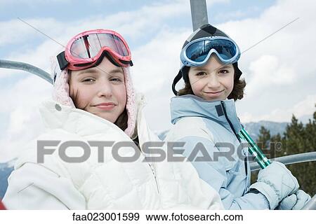 Stock Photo - Teenage girl and younger friend taking ski lift, portrait. Fotosearch