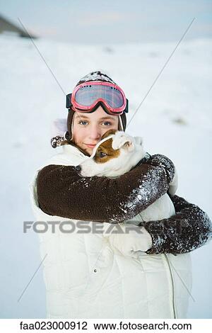 Stock Image - Teenage girl embracing dog, dressed in winter clothing, smiling at camera, portrait. Fotosearch