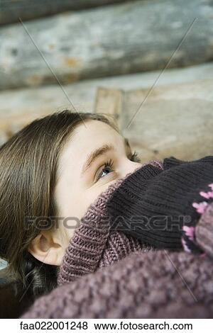 Stock Photo - Teenage girl holding edge of sweater neck over face, looking up, close-up. Fotosearch