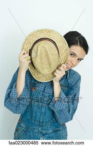 Teenage girl holding hat in front of face, smiling at camera View Large Photo Image Stock Photography - Teenage girl holding hat in front of face, smiling at camera. Fotosearch
