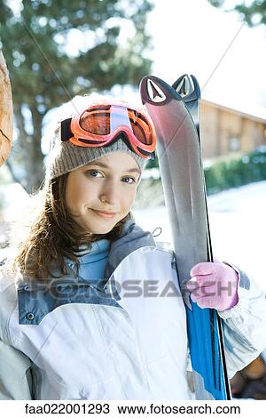 Stock Image - Teenage girl holding skis, portrait. Fotosearch