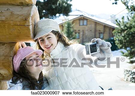 Stock Photo - Teenage girl holding up digital camera, photographing self with friend, both smiling. Fotosearch