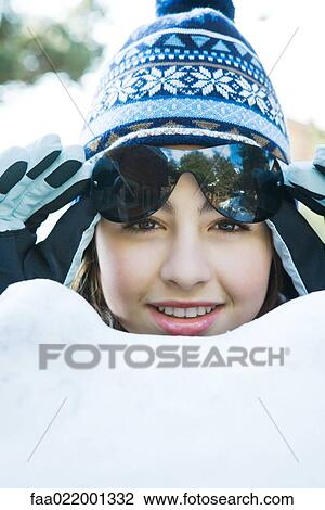 Stock Image - Teenage girl in snow, wearing winter clothes, lifting sunglasses, portrait. Fotosearch