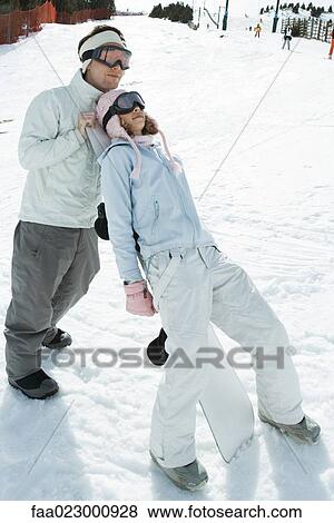 Teenage girl leaning against snowboard, male friend standing behind, full length View Large Photo Image Stock Photo - Teenage girl leaning against snowboard, male friend standing behind, full length. Fotosearch