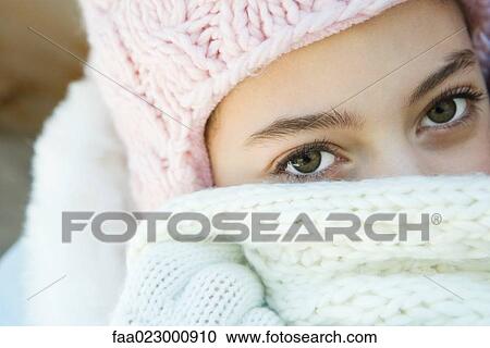 Stock Image - Teenage girl looking at camera, covering mouth with scarf, portrait. Fotosearch