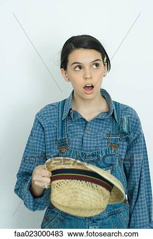 Stock Image - Teenage girl looking up, wide eyes, open mouth, holding hat. Fotosearch