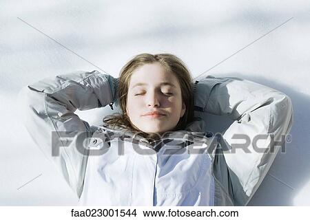 Picture - Teenage girl lying on snow with hands behind head and eyes closed. Fotosearch