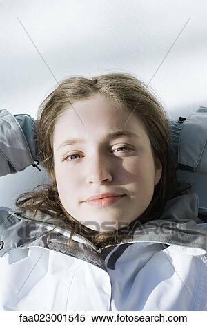 Stock Photography - Teenage girl lying on snow with hands behind head, looking at camera. Fotosearch