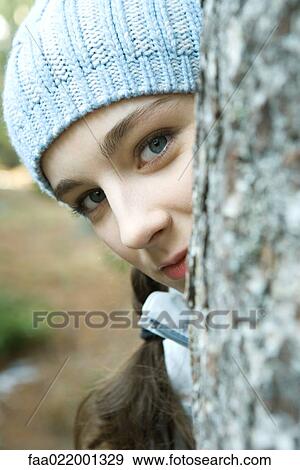 Teenage girl peeking around tree trunk, looking at camera, portrait View Large Photo Image Stock Photo - Teenage girl peeking around tree trunk, looking at camera, portrait. Fotosearch