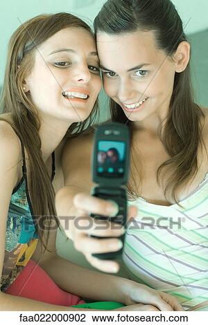 Teenage girl photographing self and friend with cell phone, both smiling View Large Photo Image Stock Image - Teenage girl photographing self and friend with cell phone, both smiling. Fotosearch