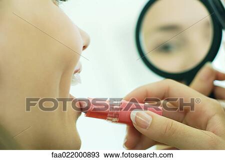 Teenage girl putting on lipstick, looking at self in hand mirror, cropped view View Large Photo Image Stock Image - Teenage girl putting on lipstick, looking at self in hand mirror, cropped view. Fotosearch
