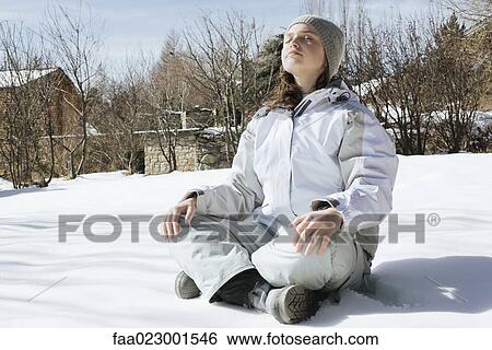 Stock Photograph - Teenage girl sitting indian style on snow with eyes closed and head back, full length. Fotosearch