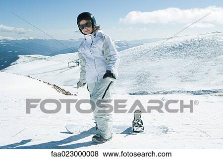 Stock Photo - Teenage girl standing with snowboard, smiling at camera, full length portrait. Fotosearch