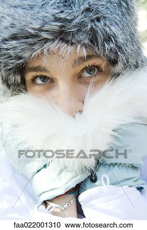 Stock Image - Teenage girl wearing fur hat, pushing fur collar over mouth, close-up portrait. Fotosearch