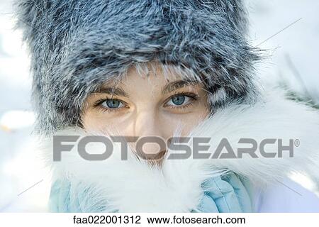 Stock Image - Teenage girl wearing fur hat, pushing fur collar over mouth, close-up portrait. Fotosearch
