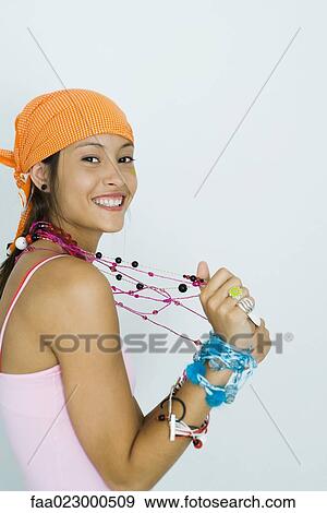 Stock Photo - Teenage girl wearing lots of jewelry, smiling at camera, portrait. Fotosearch